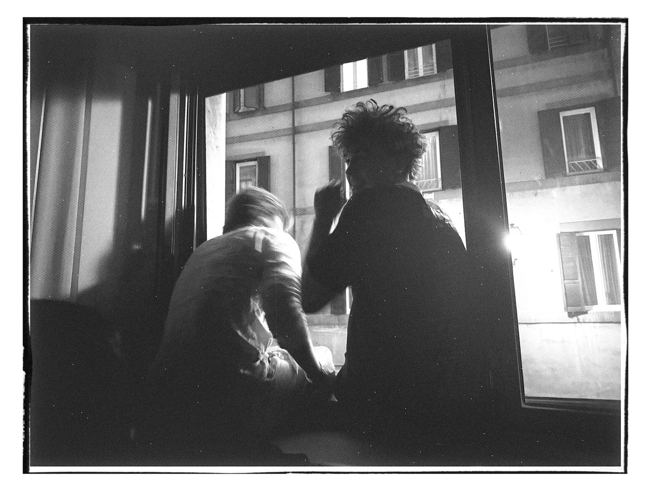 Two figures silhouetted in a window at night, shot on black and white film