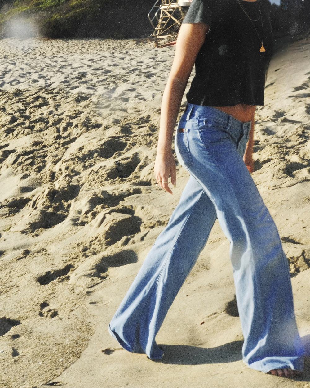 Cropped at the shoulders, mid-stride across the sand in light flared denim