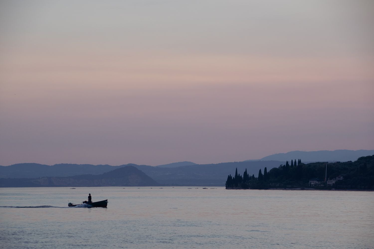 A lone boat crossing a lake at dusk beneath pink and grey hills