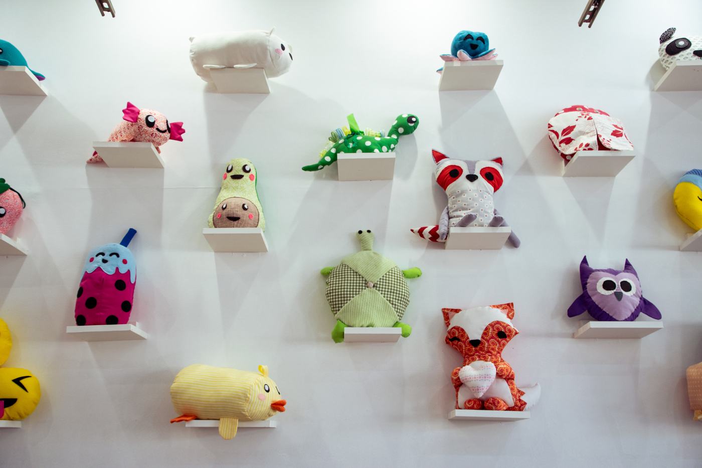 A wall of handmade plush animals on white shelves