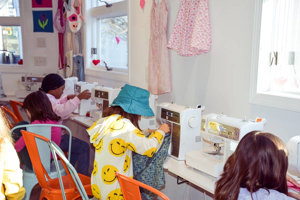 A row of sewing machines in use along a sunlit studio window