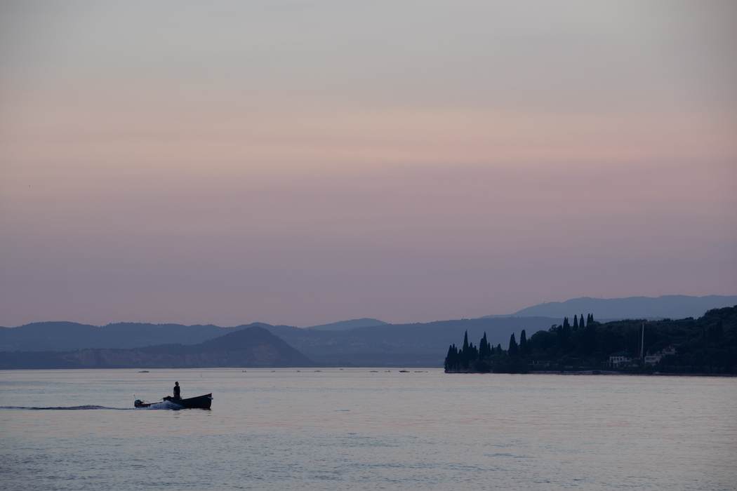 A lone boat crossing a lake at dusk beneath pink and grey hills