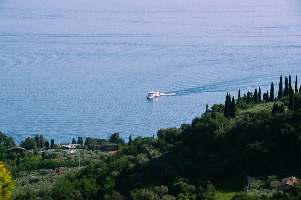 A ferry crossing Lake Garda seen from a hillside of cypress and olive trees
