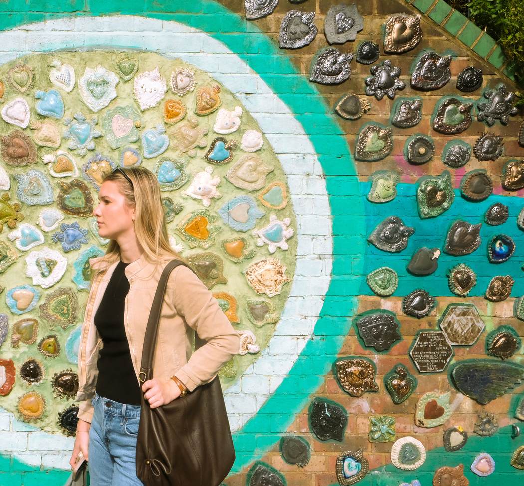 A figure walking past a wall of ceramic hearts painted in turquoise, London