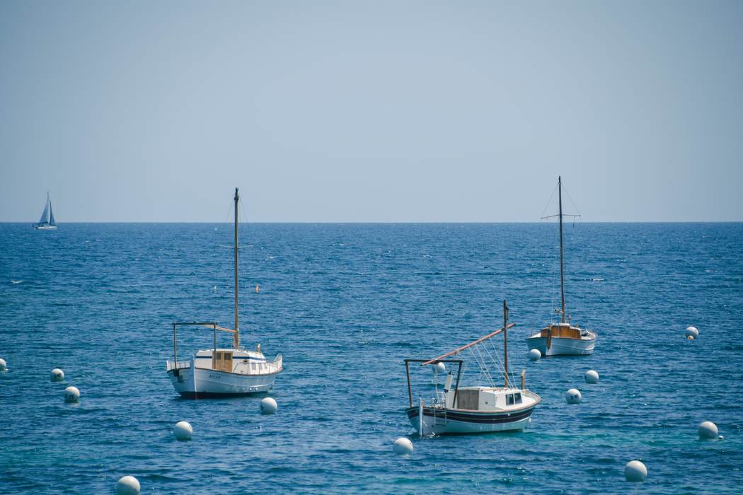 Three wooden boats moored on flat blue sea