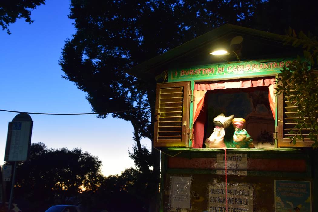 A lit puppet theatre performing against a deep blue dusk sky in Rome