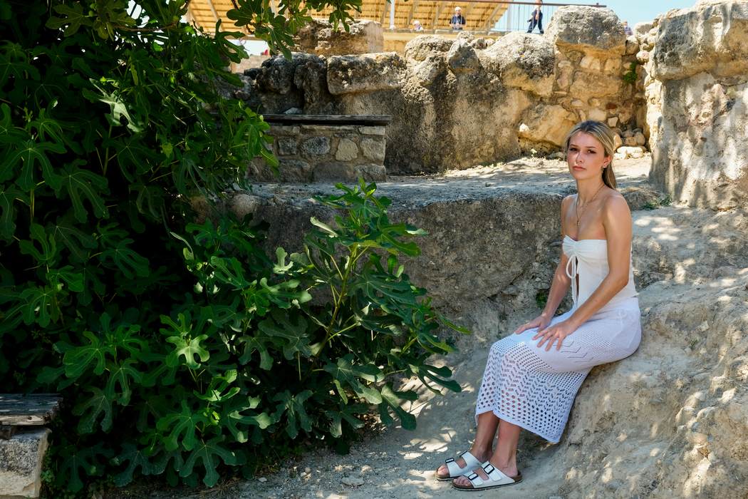 A figure seated among sunlit ruins beside a fig tree
