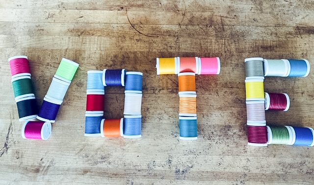 The word VOTE spelled out in spools of colored sewing thread on a wooden table